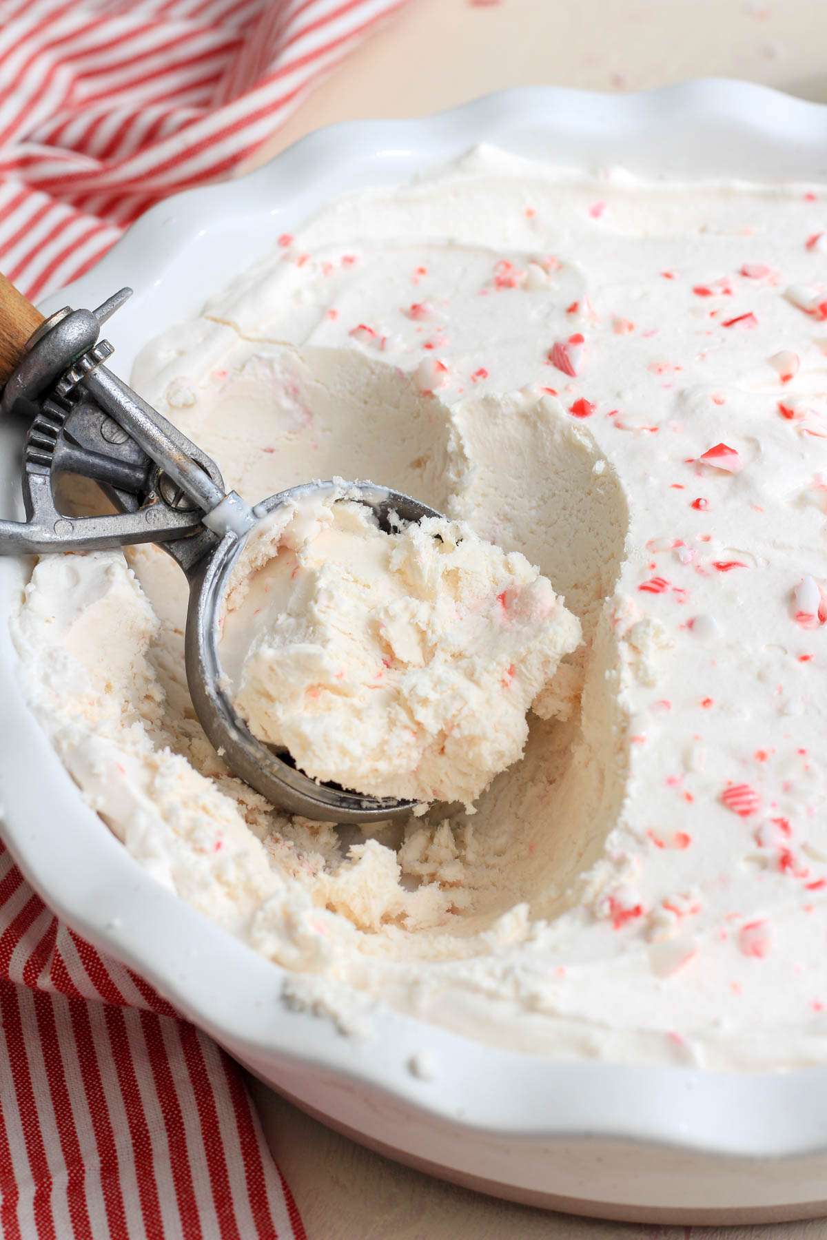 The silver part of an ice cream scoop filled with no churn peppermint ice cream in a white dish of ice cream.
