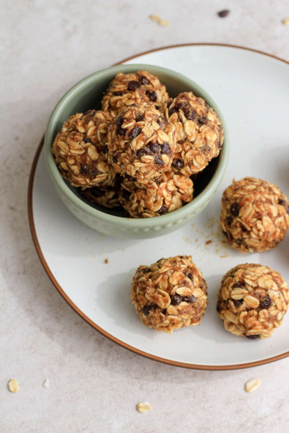 Dairy-free peanut butter chocolate chip lactation bites in a small green bowl on a white plate with three more bites on the plate.
