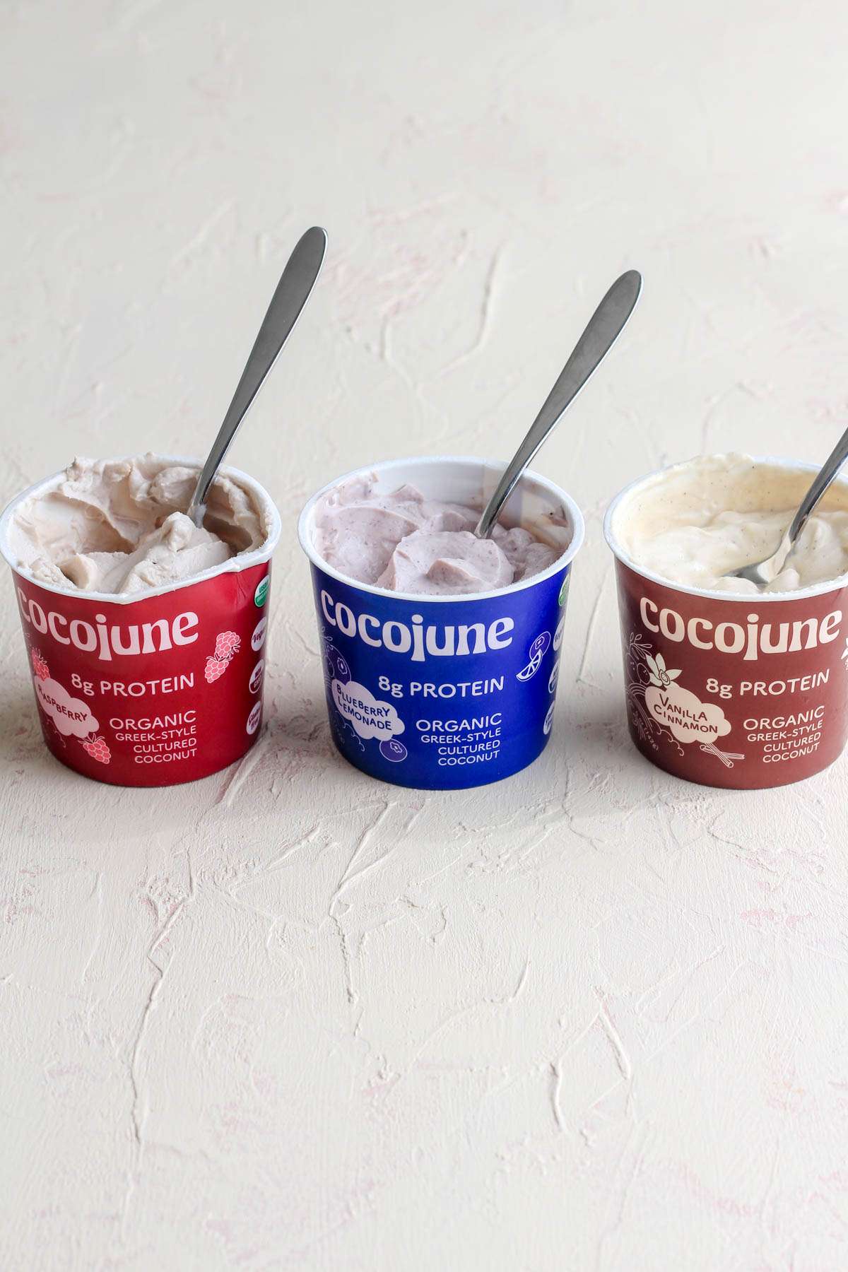 A cream counter with three flavors of coocjune greek-style yogurt with spoons sticking out.