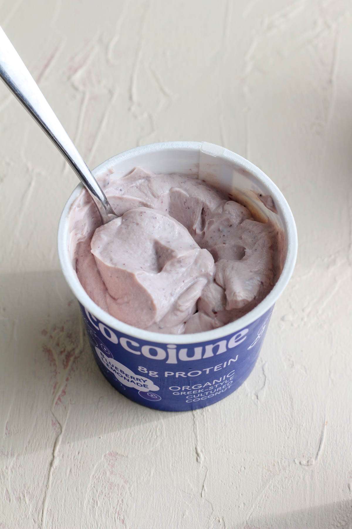A blueberry lemonade cocojune with a silver spoon in the left side of the carton.
