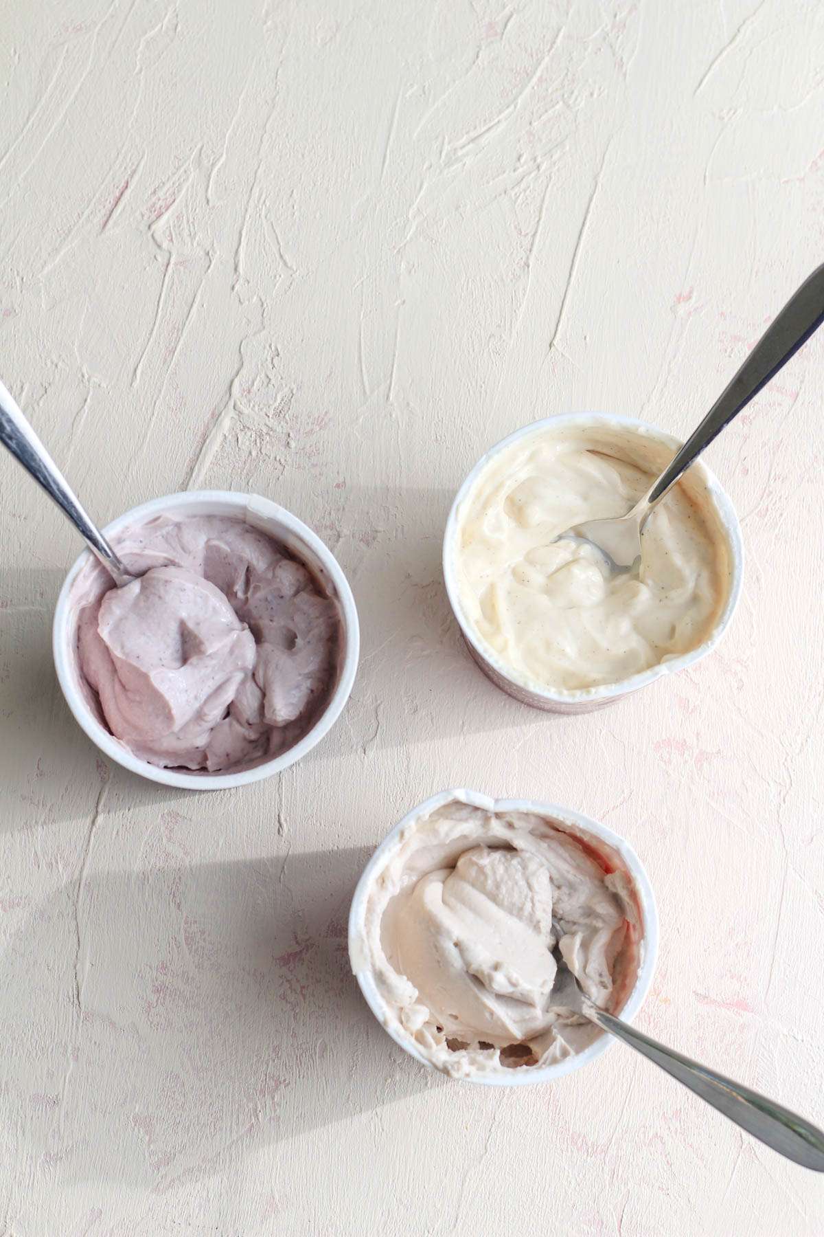 A top down image of three cartons of cocojune yogurt with spoons inside.