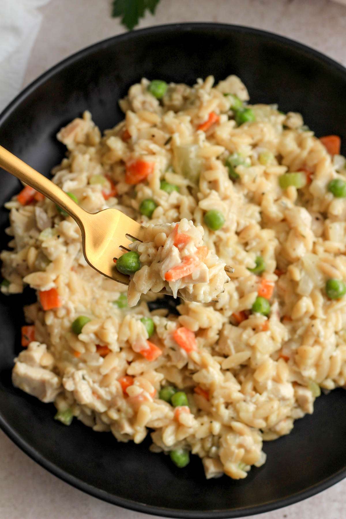 A top down image of chicken pot pie orzo on a gold fork over a black bowl of the dairy-free orzo.