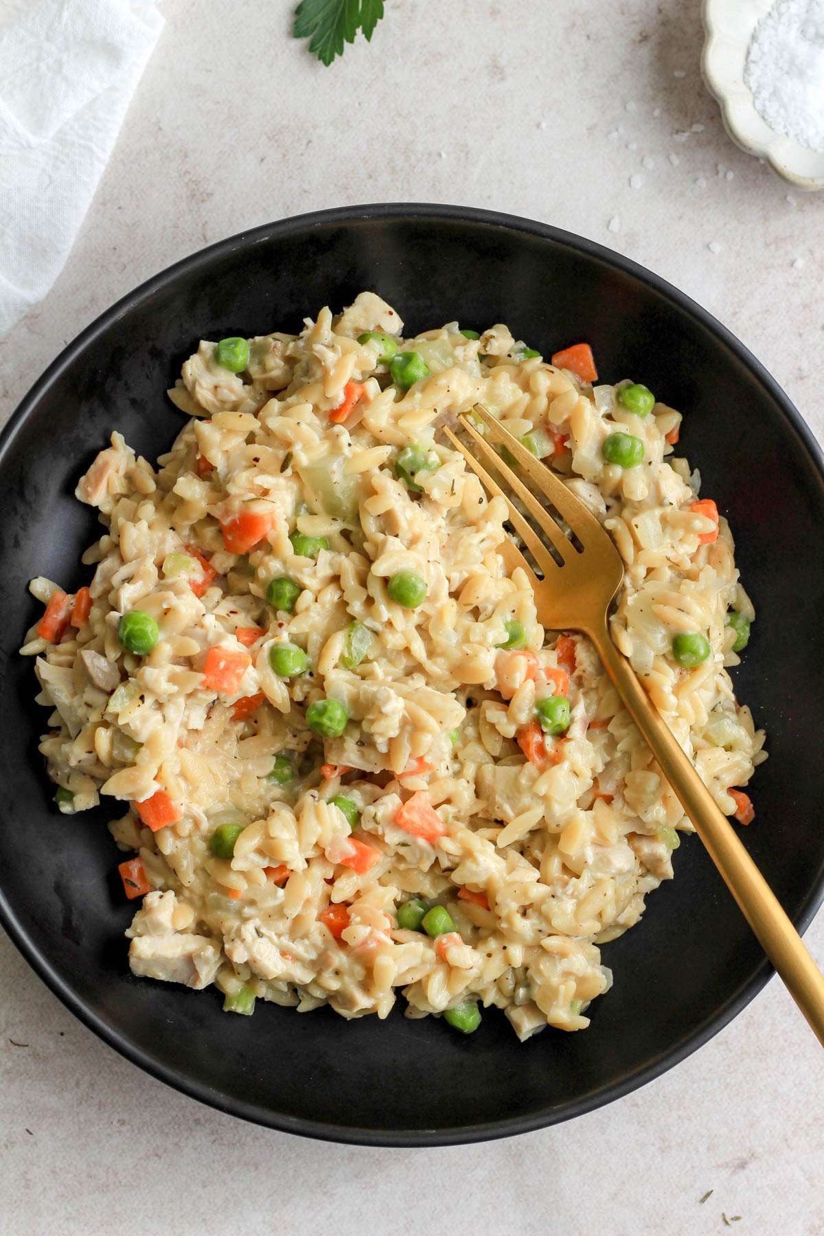 A black bowl of dairy free chicken pot pie orzo with coconut milk with a gold fork on the right side.