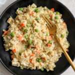 A close up of a black bowl with a gold fork in a serving of one pot chicken pot pie orzo.