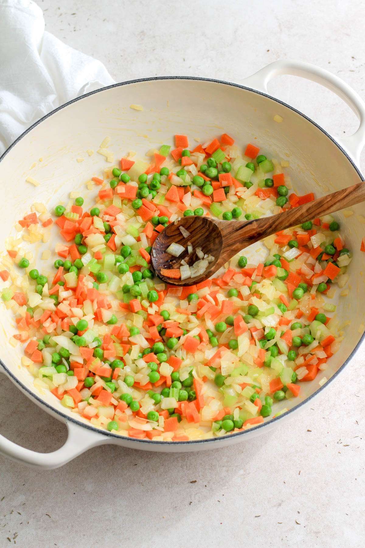 A white pan with a wooden spoon after cooking the vegetable base for the chicken pot pie orzo.