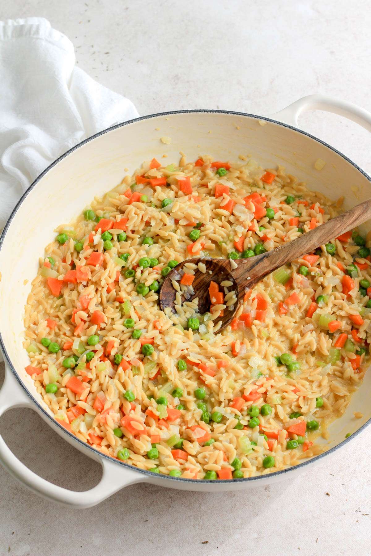 A white skillet with cooked orzo before adding coconut milk, chicken, and spices.