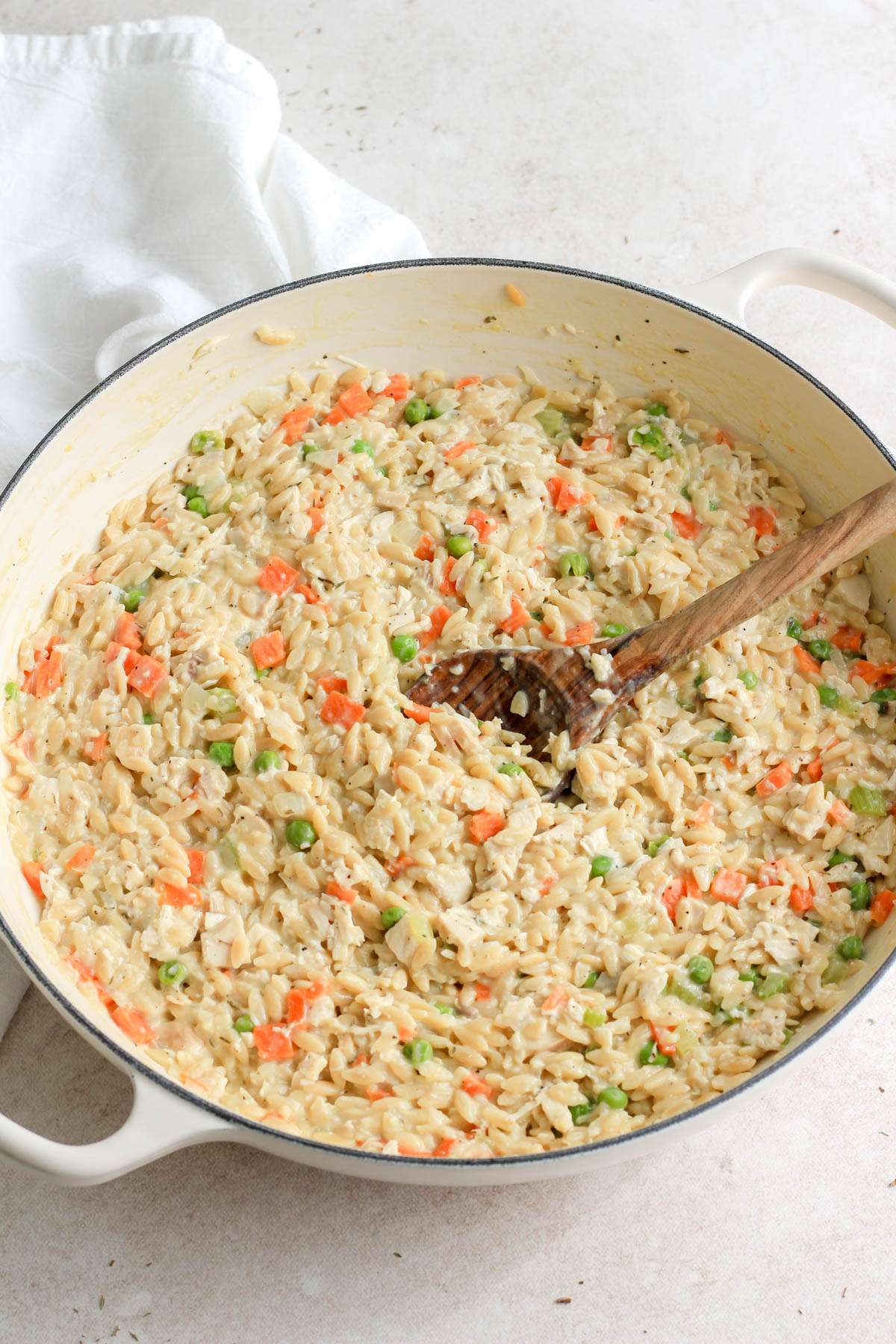 One pot dairy free chicken pot pie orzo in a white skillet with a wooden spoon.