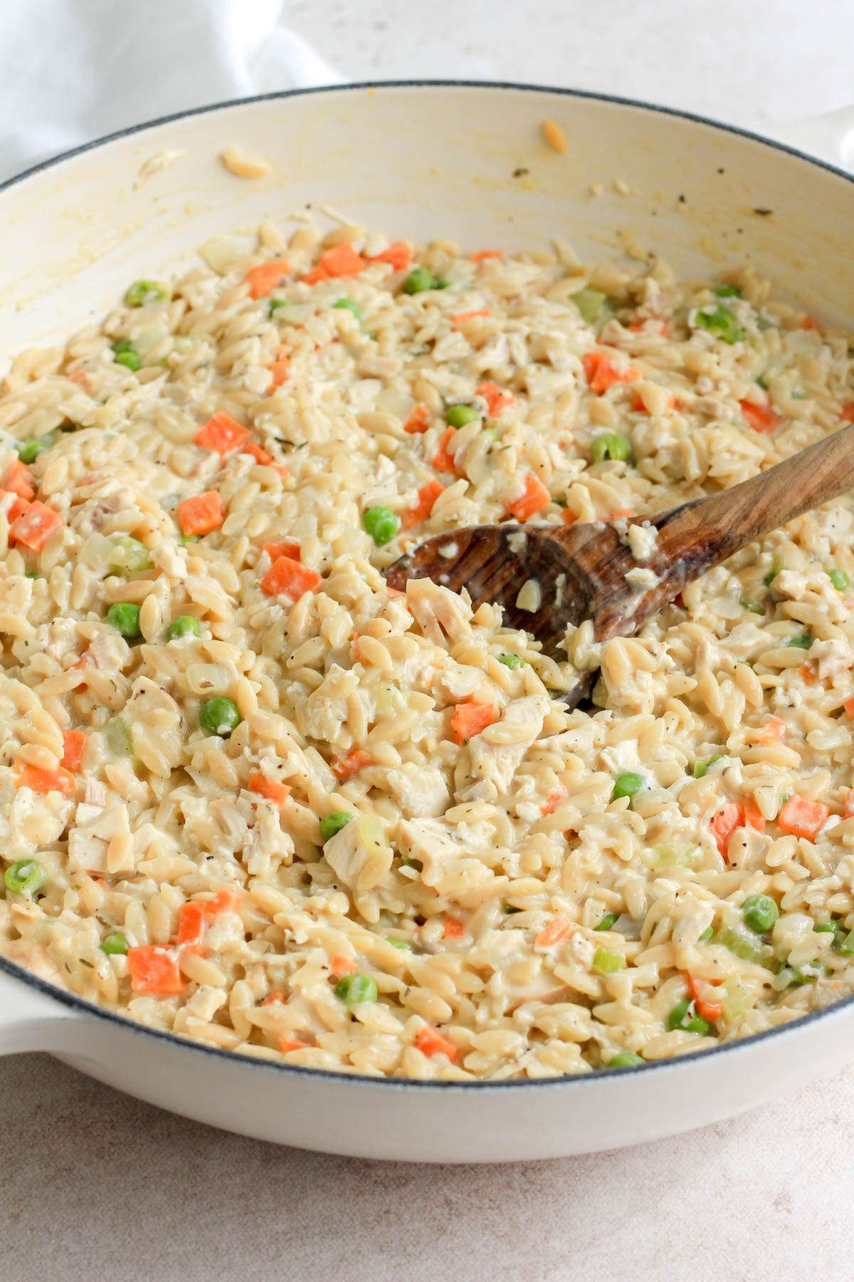 A close up of a white pan filled with dairy free chicken pot pie orzo being scooped with a wooden spoon.