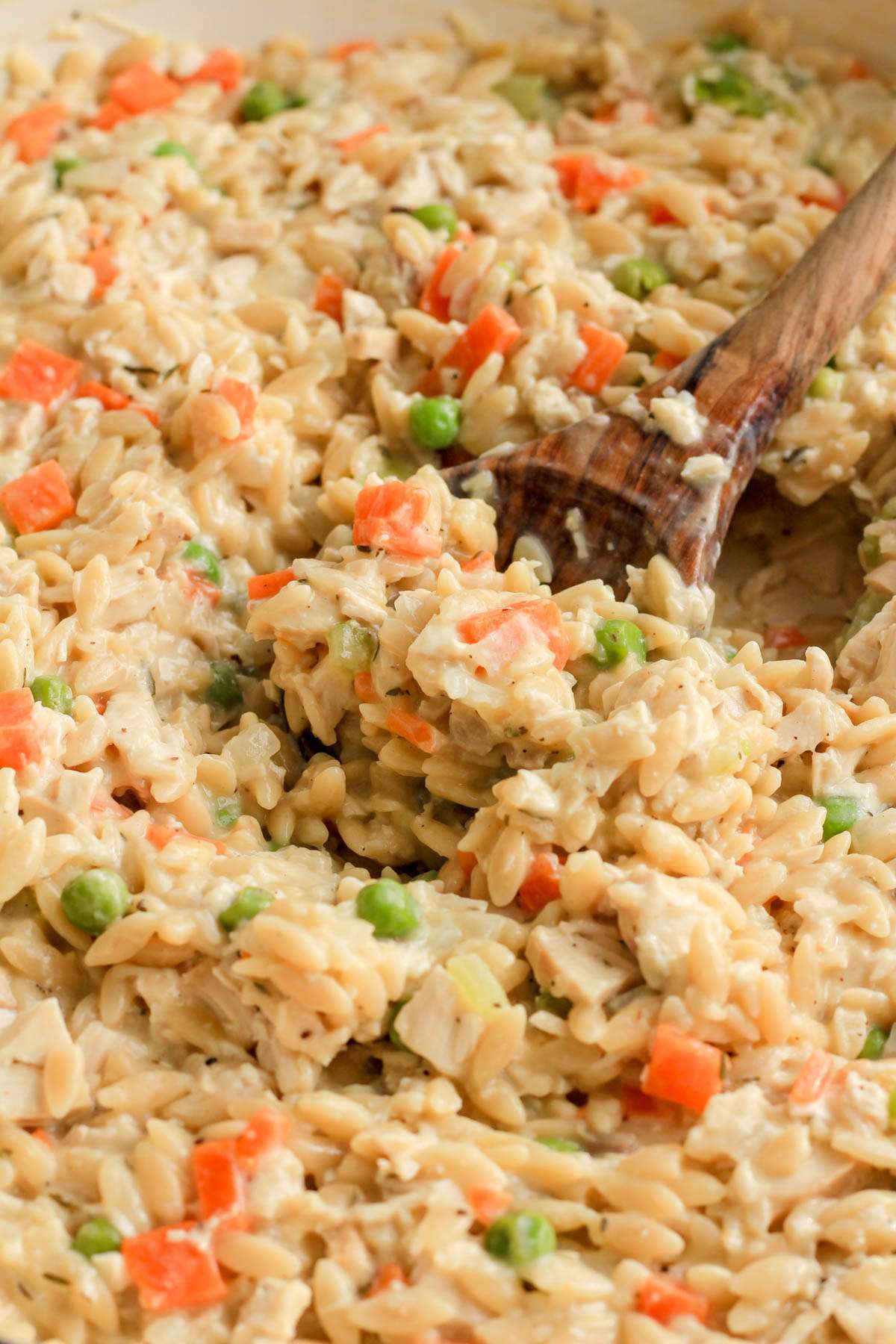 A scoop of dairy free chicken pot pie orzo in a white skillet.