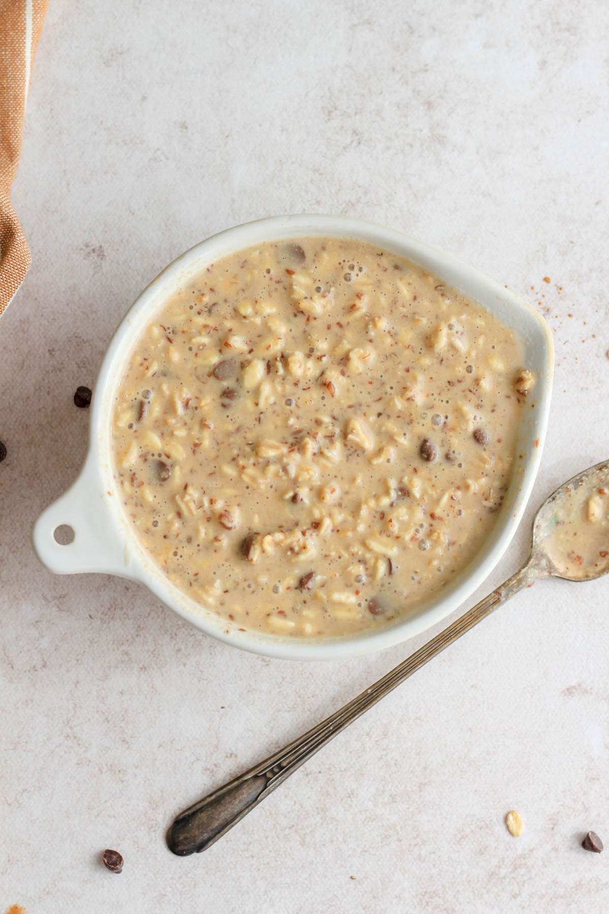A top down image of peanut butter chocolate chip lactation overnight oats in a white bowl of a cream counter.