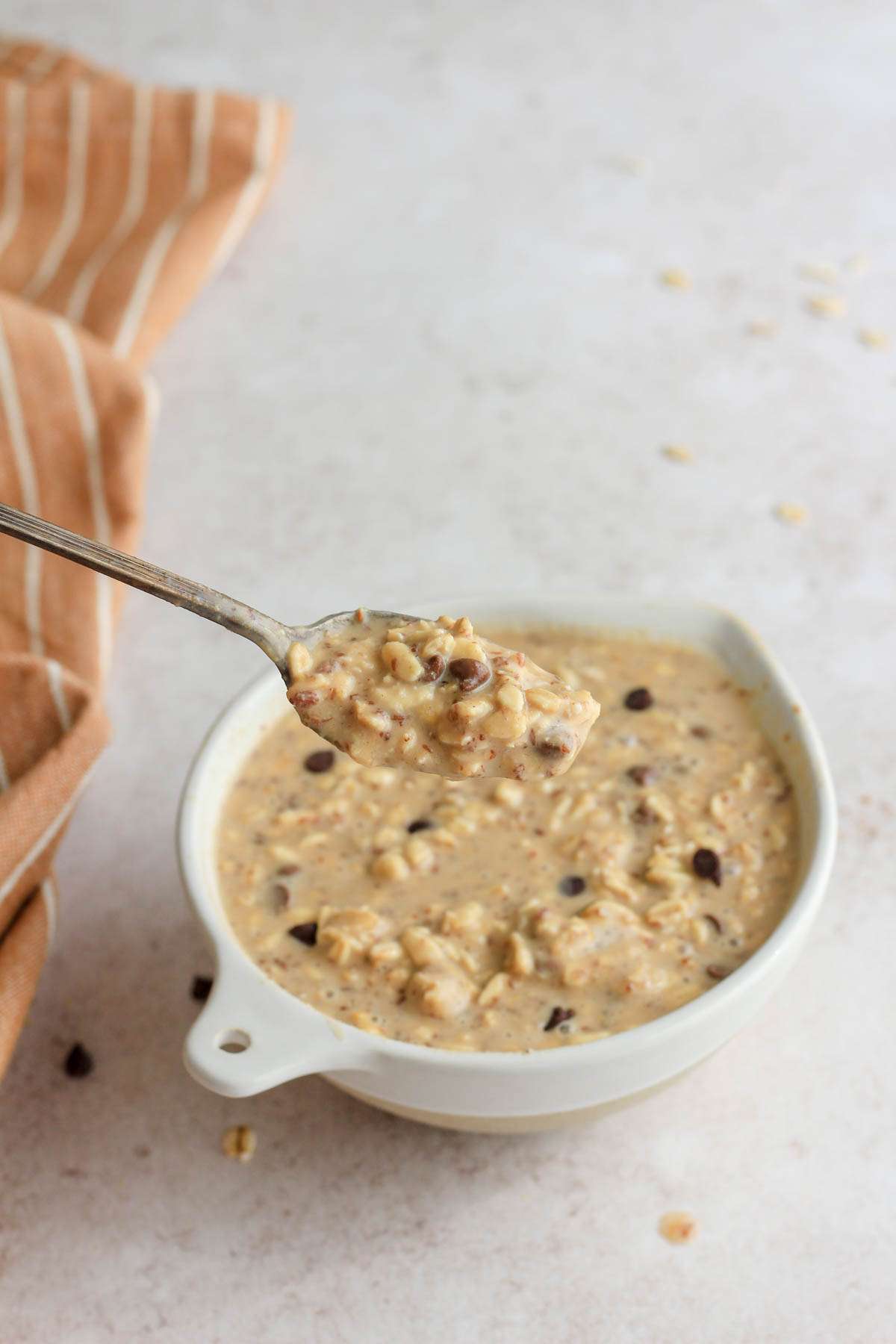 From the side, a bowl of lactation boosting overnight oats with peanut butter and chocolate chips with a silver spoon holding a scoop of the vegan oatmeal on the left side of the bowl.