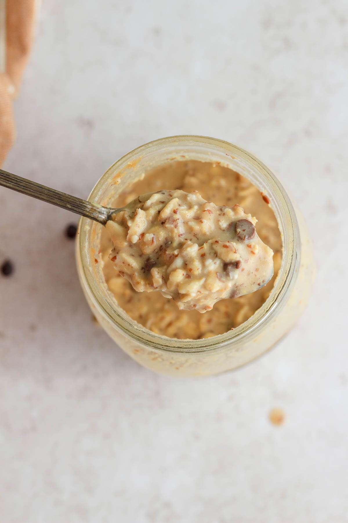 A spoon pulling a scoop of peanut butter chocolate chip lactation overnight oats out of a mason jar.