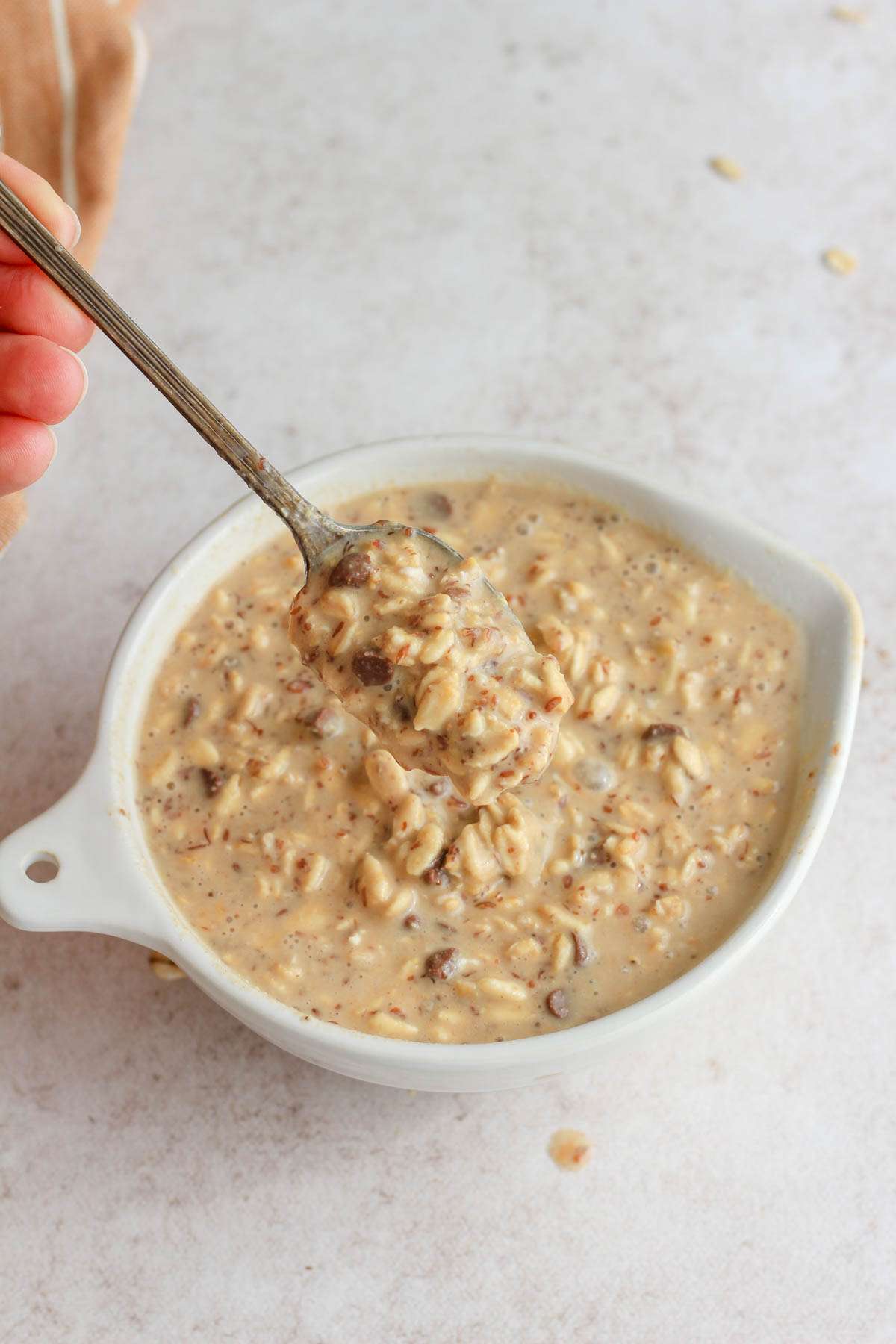A white bowl with a silver spoon scooping up lactation overnight oats.