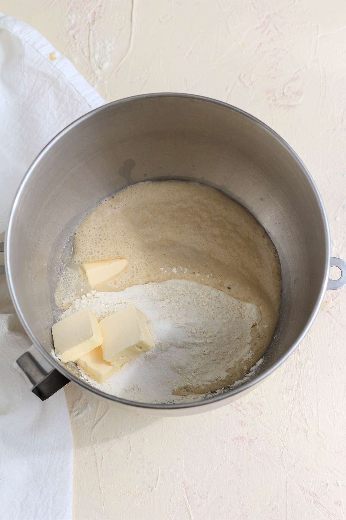 A silver mixing bowl with activated yeast, flour, salt, and chunks of vegan butter.