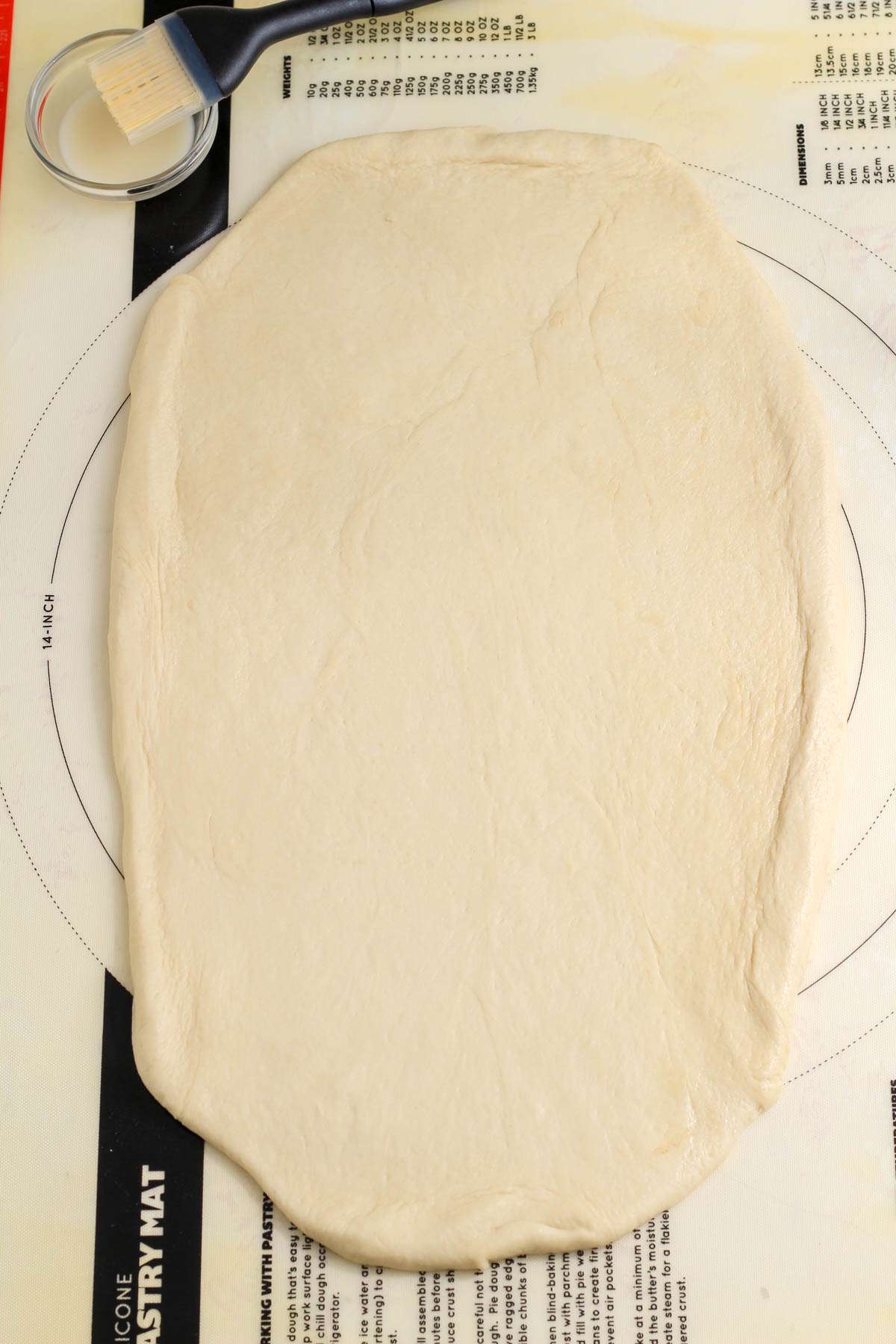 A pastry mat with a rolled out rectangle of bread dough.