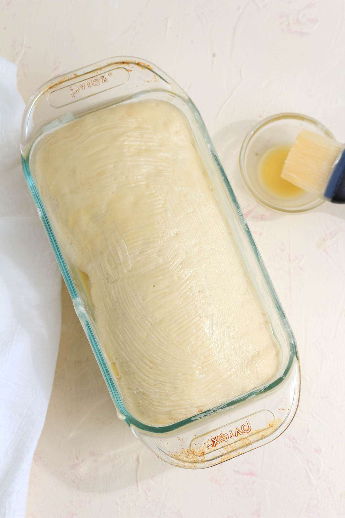 A glass bread loaf with a small glass bowl of melted vegan butter in the upper right corner.