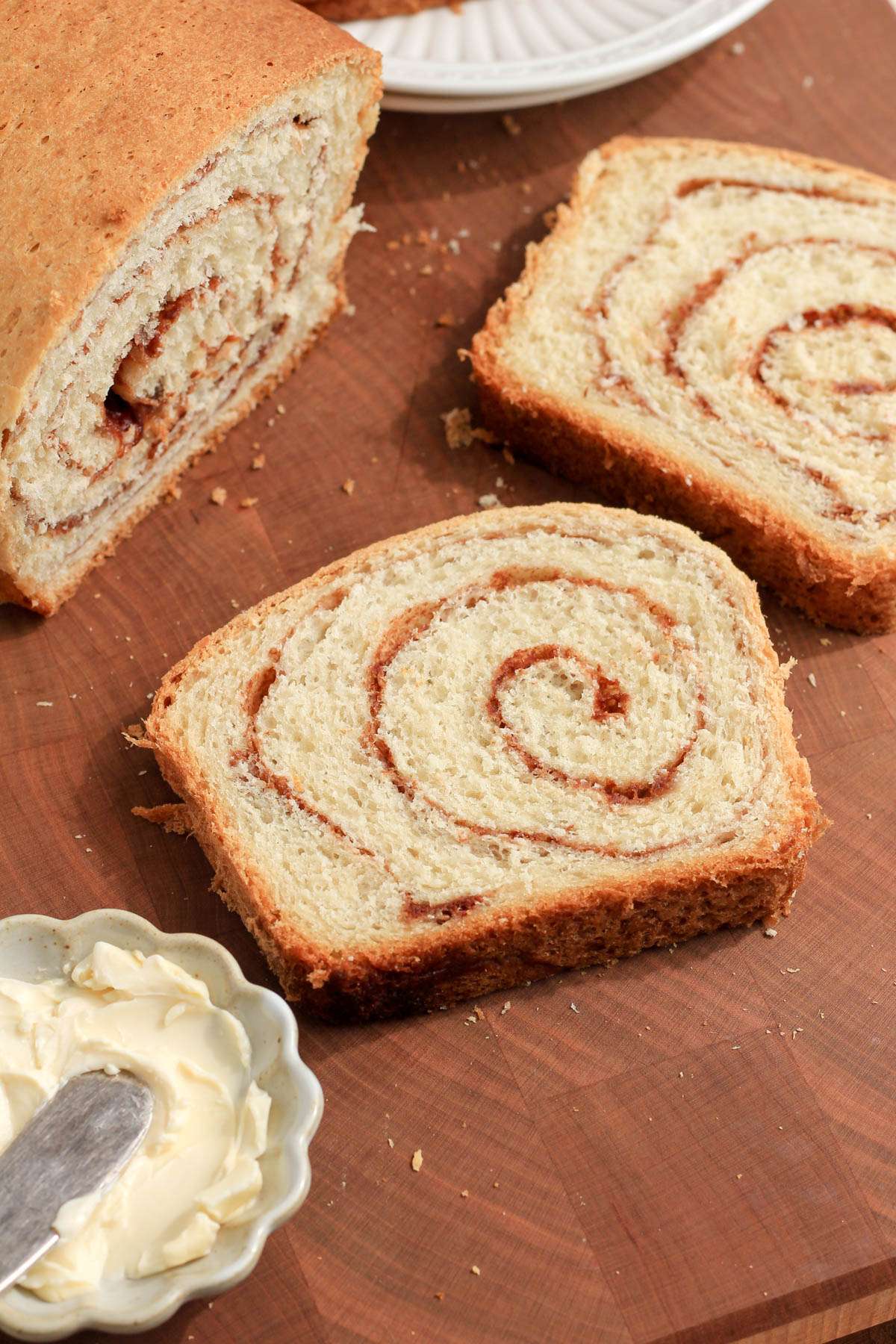 A wooden cutting board with two sliced of cinnamon swirl bread with a small dish of vegan butter in the bottom left.