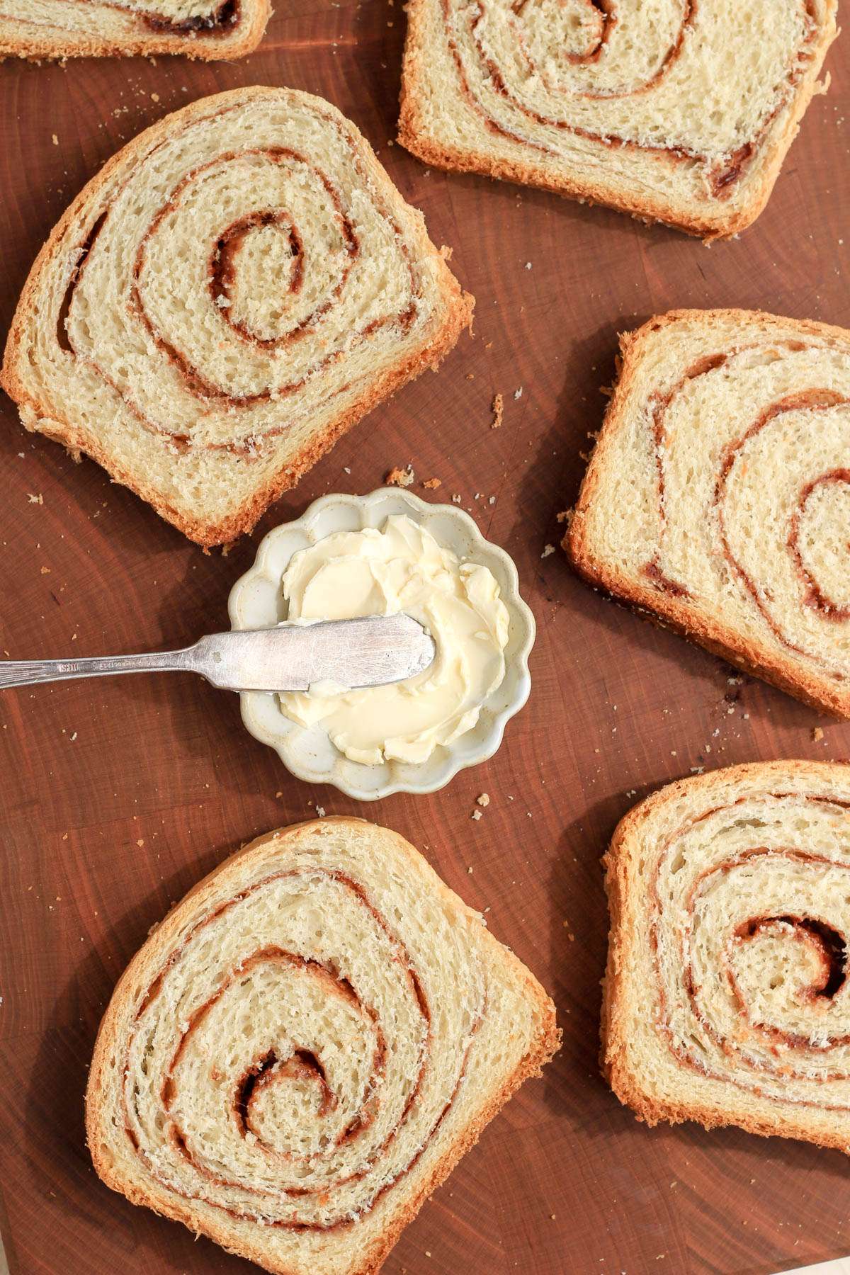 A wooden cutting board with sliced of vegan cinnamon swirl bread with a small dish of vegan butter in the middle.