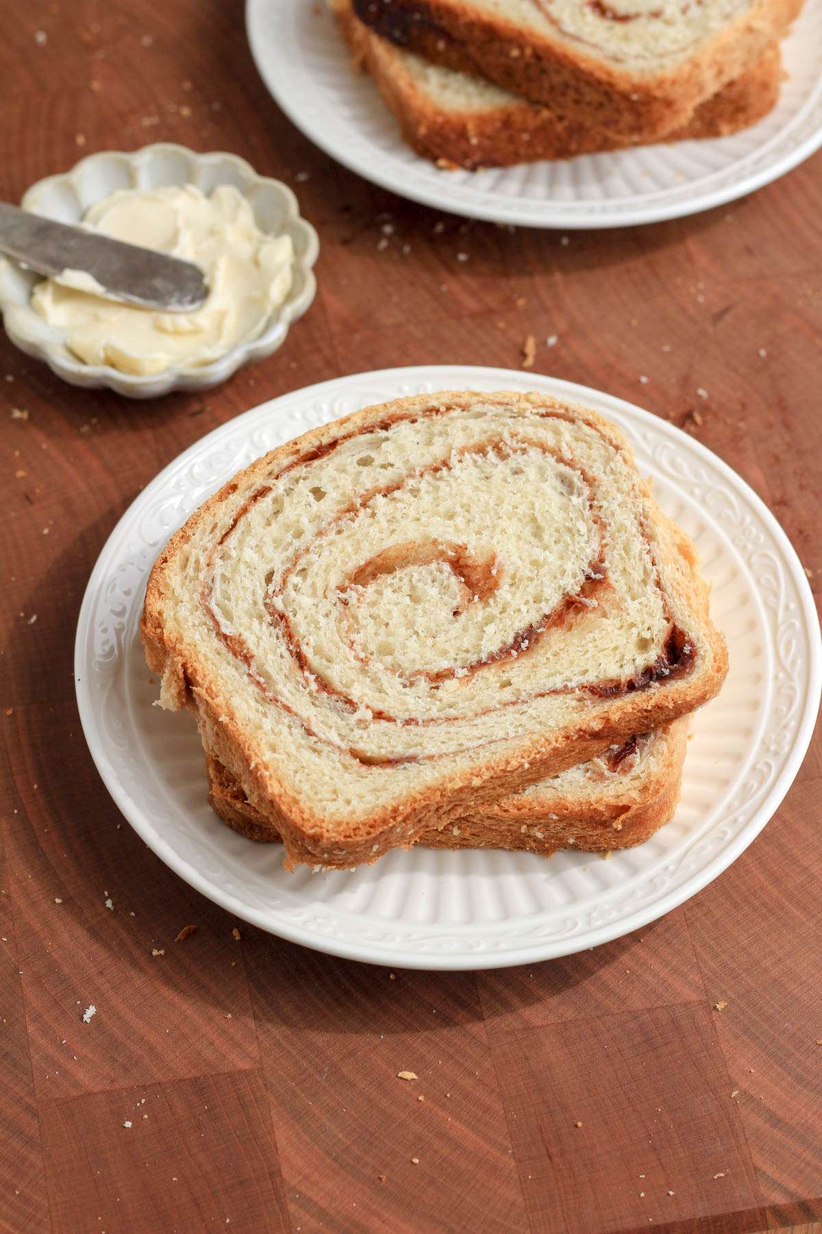 A small white plate with two slices of vegan cinnamon bread on a wooden cutting board.