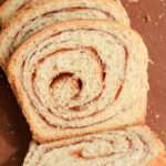 A close up of a slice of vegan cinnamon swirl bread on a wooden cutting board.