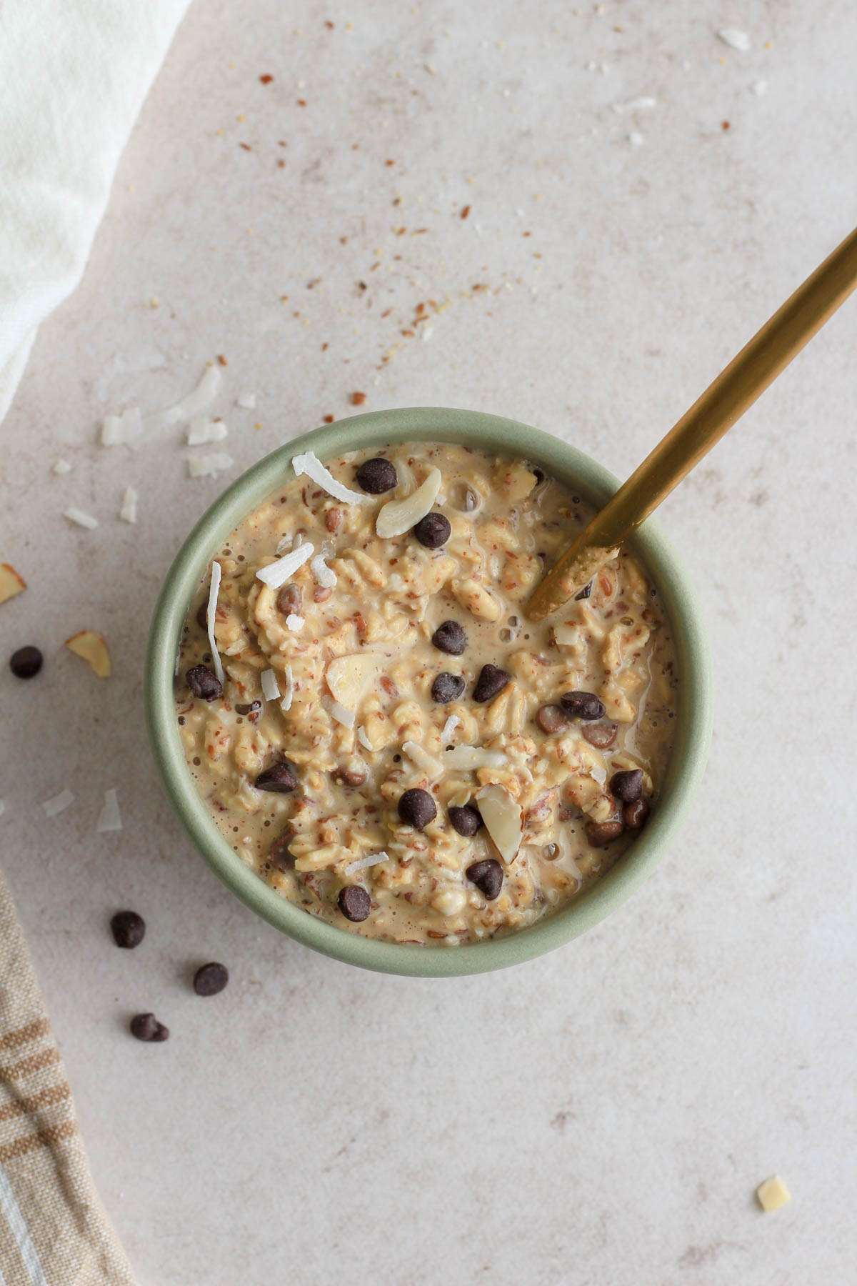 A top down image of a green bowl of almond joy lactation overnight oats with a gold spoon in the top right side.