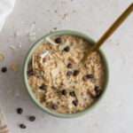 A close up of a green bowl of vegan almond joy overnight oats topped with chocolate, coconut, and almond slices.