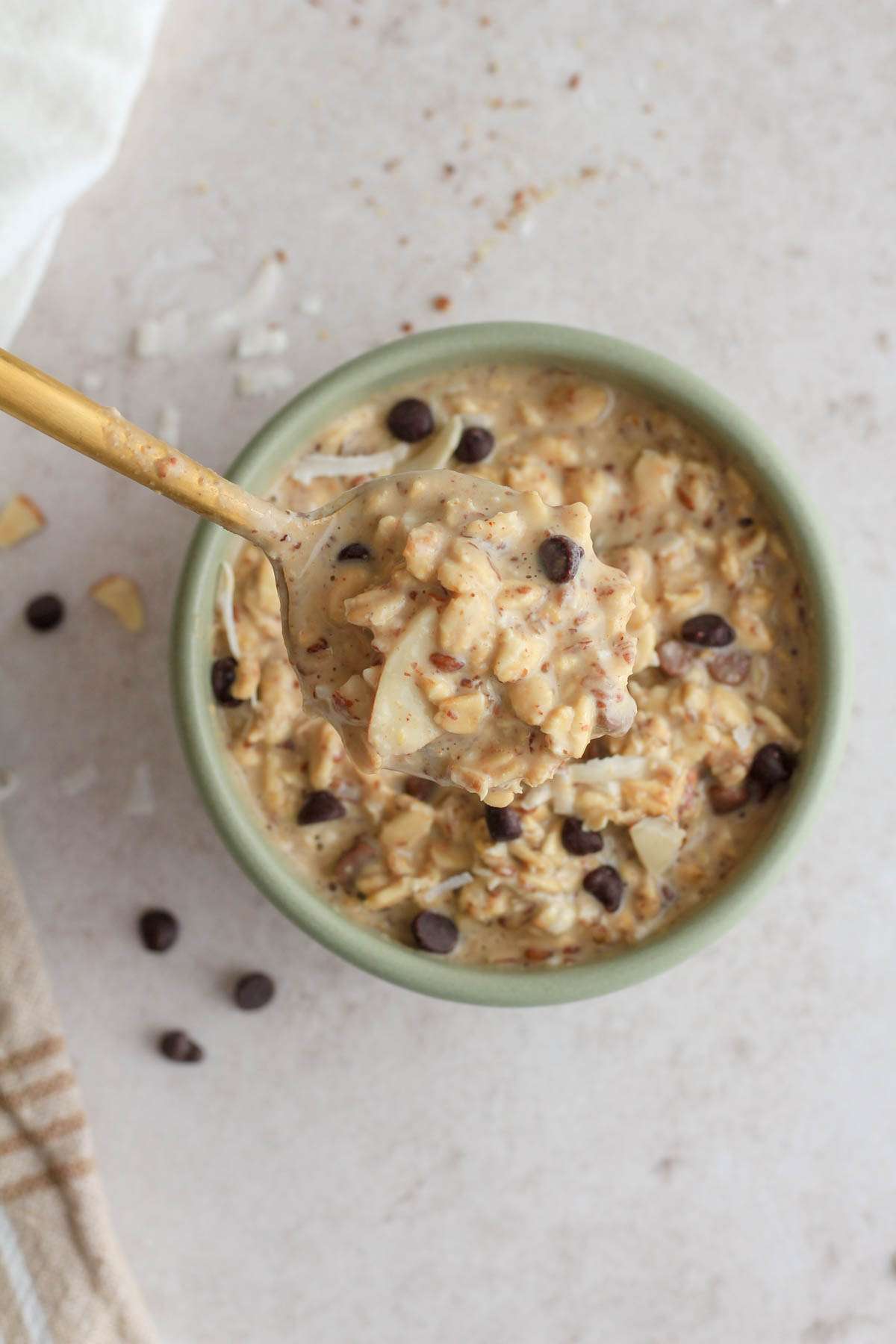 A gold spoon lifting a scoop of overnight oats out of a green bowl.