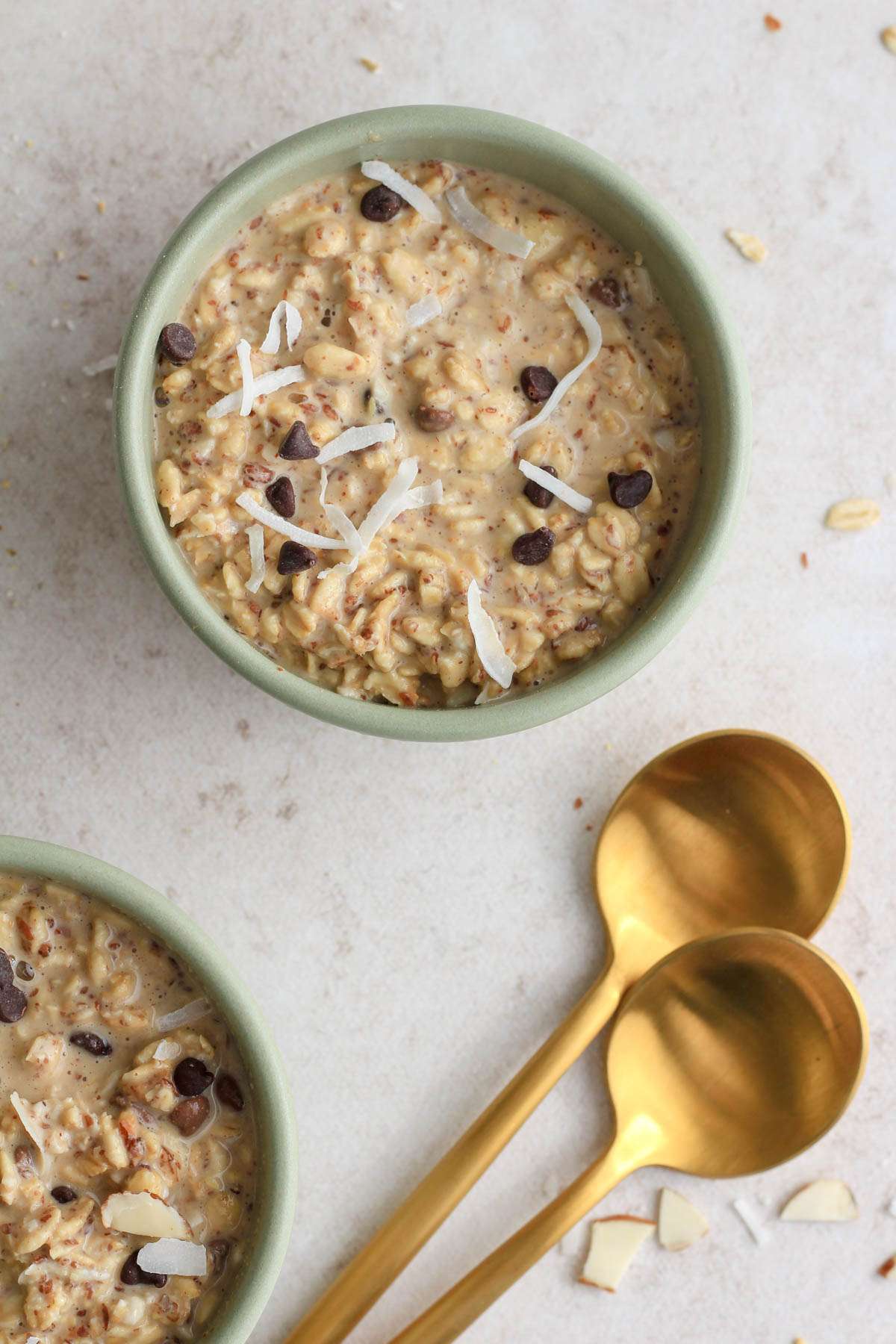 A top down image of two green bowls of lactation overnight oats next to two gold spoons.