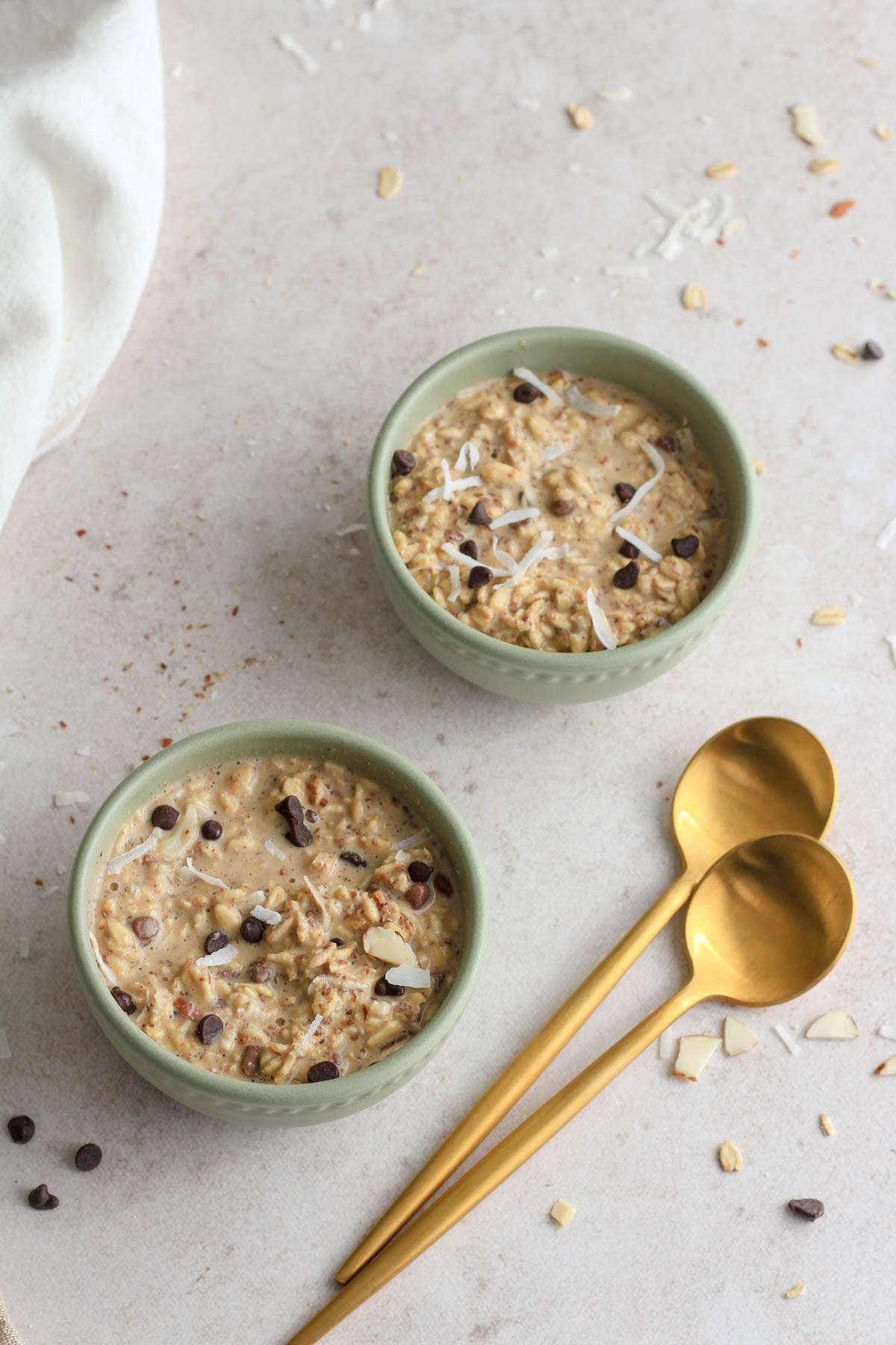 Two green bowls of overnight oatmeal on a tan counter next to a set of gold spoons.