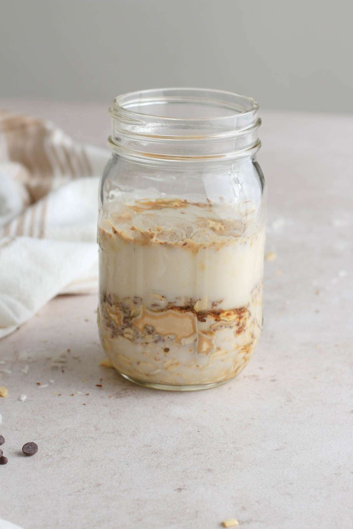 A glass mason jar with the ingredients for lactation overnight oats before mixing.