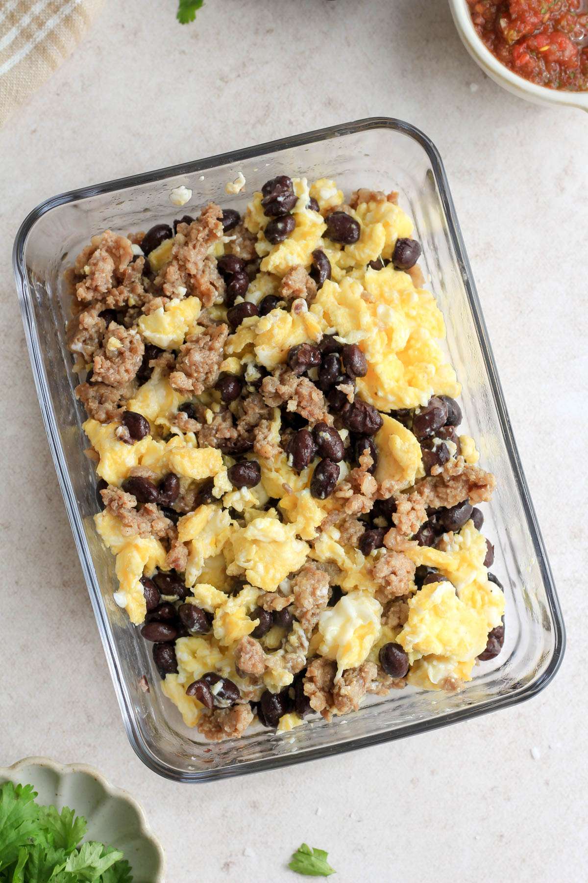Black bean, eggs, and sausage scramble in a rectangular meal prep container on a tan counter.