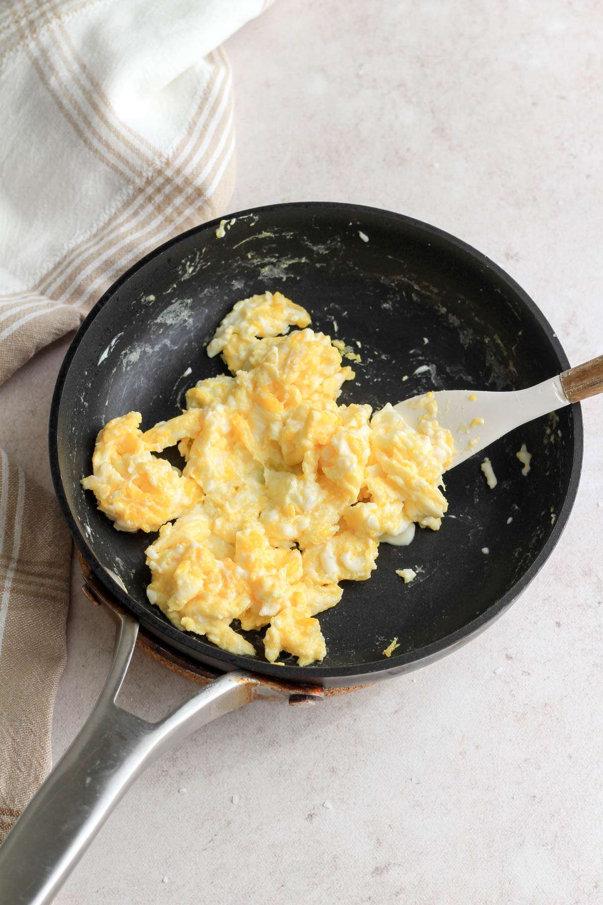 A non-stick skillet with a wooden and white spatula after cooking three eggs.