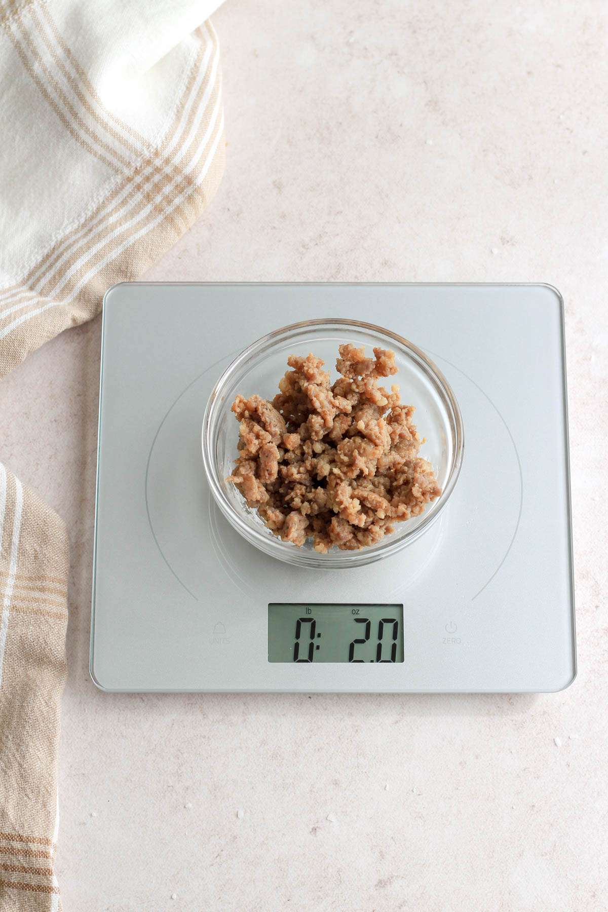 A kitchen scale with a small bowl of breakfast sausage measured at 2 ounces.