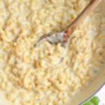 A close up of a wooden spoon in a white skillet with dairy-free boursin sauce coated pasta.