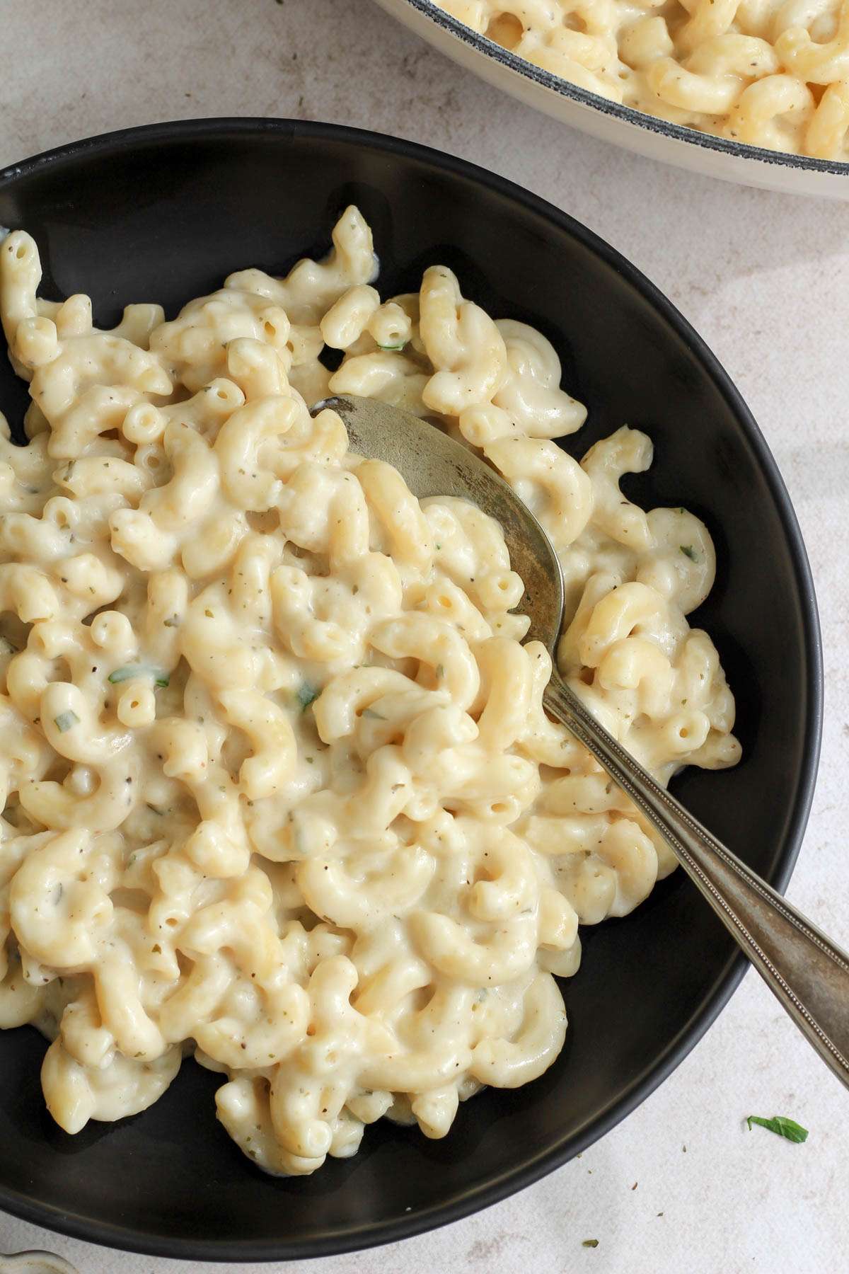A top down image of a black bowl with vegan boursin pasta with a silver spoon on the right side.