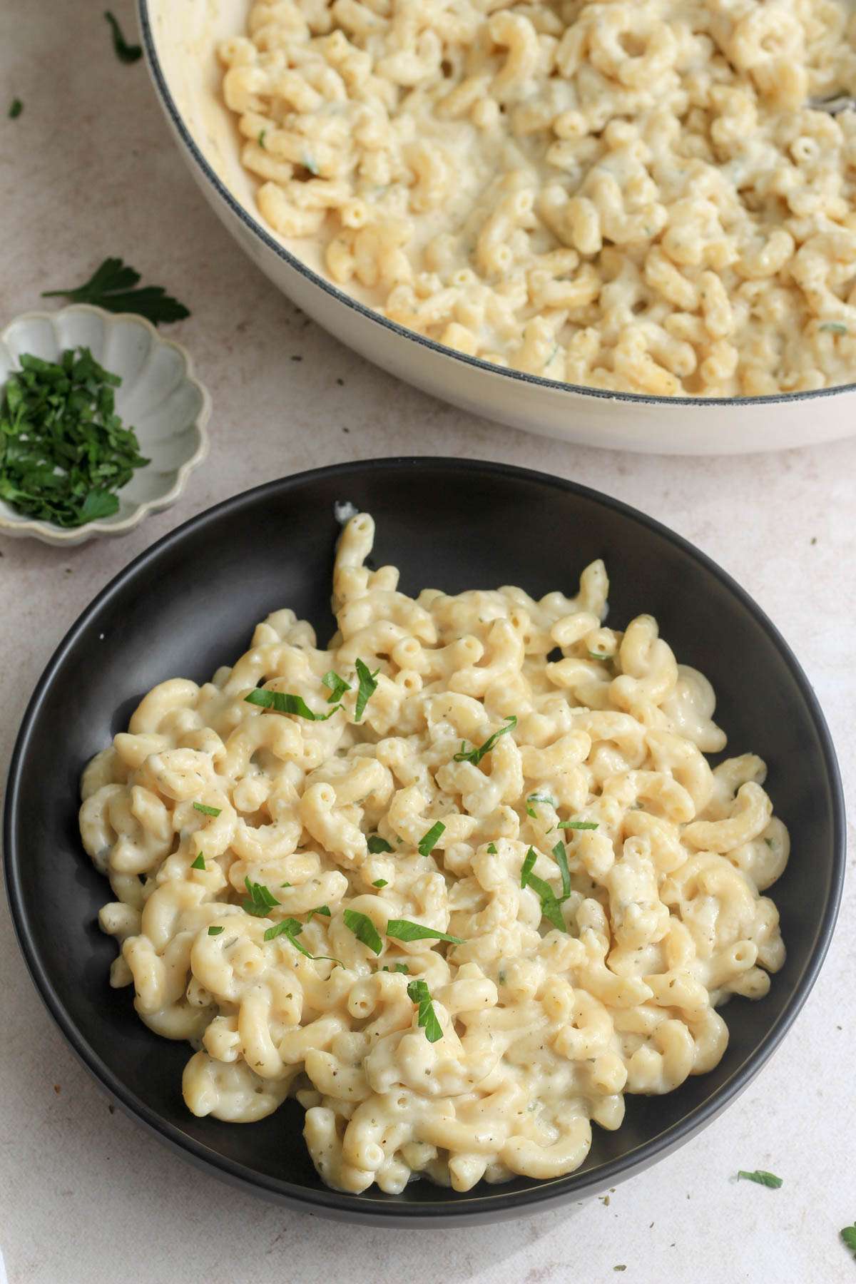 A black bowl of boursin sauce pasta in front of a white skillet with more pasta.