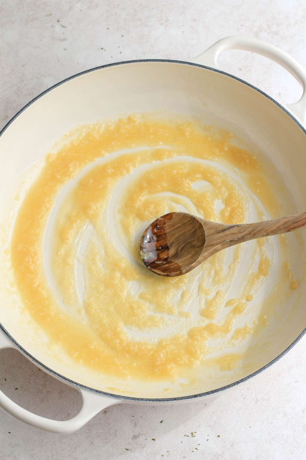 A white skillet with a wooden spoon making a roux.