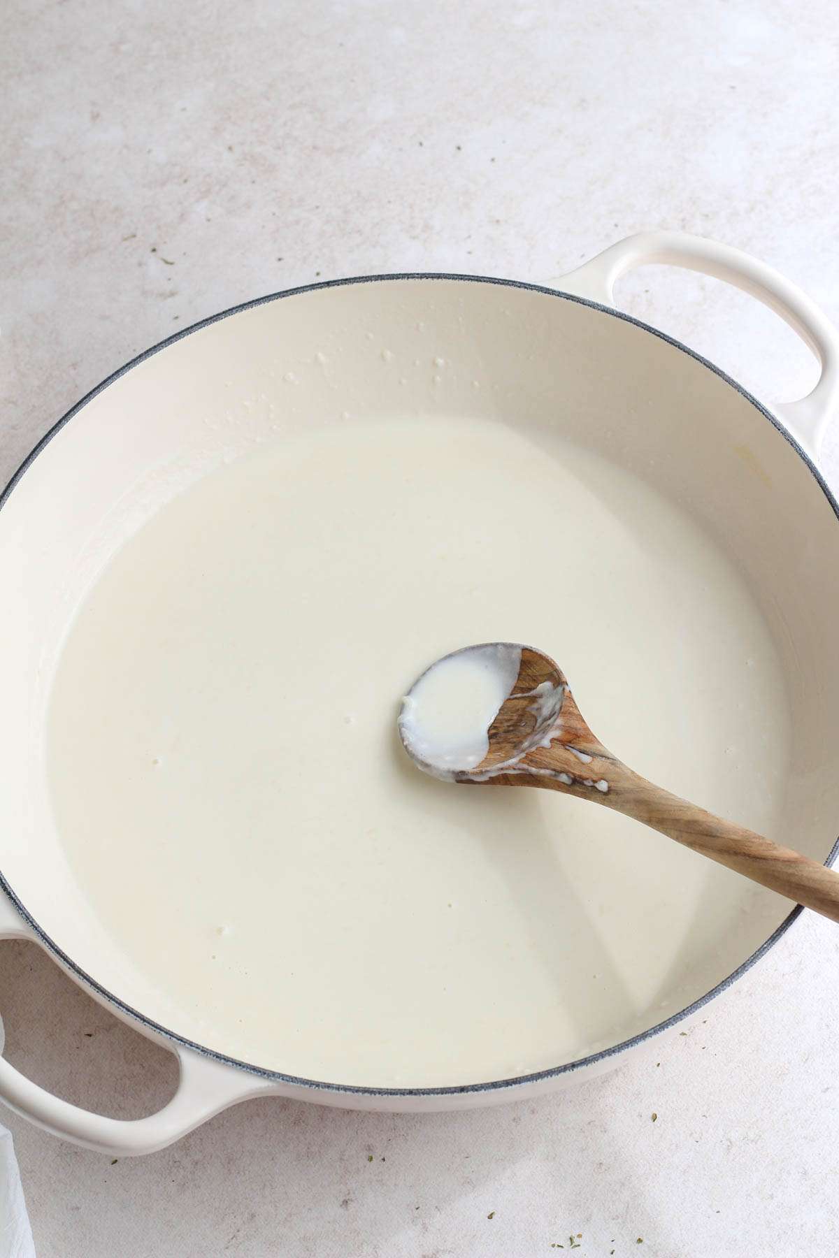 A white skillet with a wooden spoon after adding coconut milk to the roux.