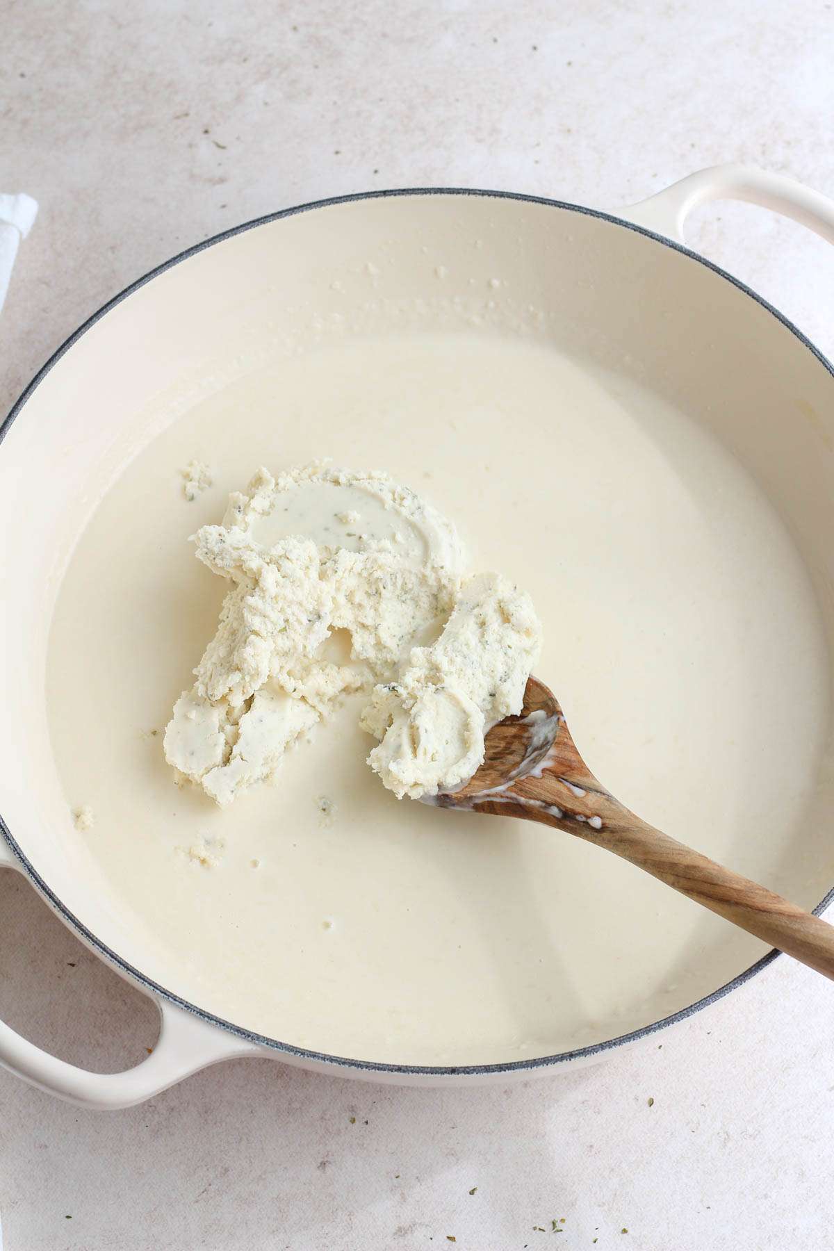 A white skillet with a wooden spoon stirring in the vegan boursin cheese.