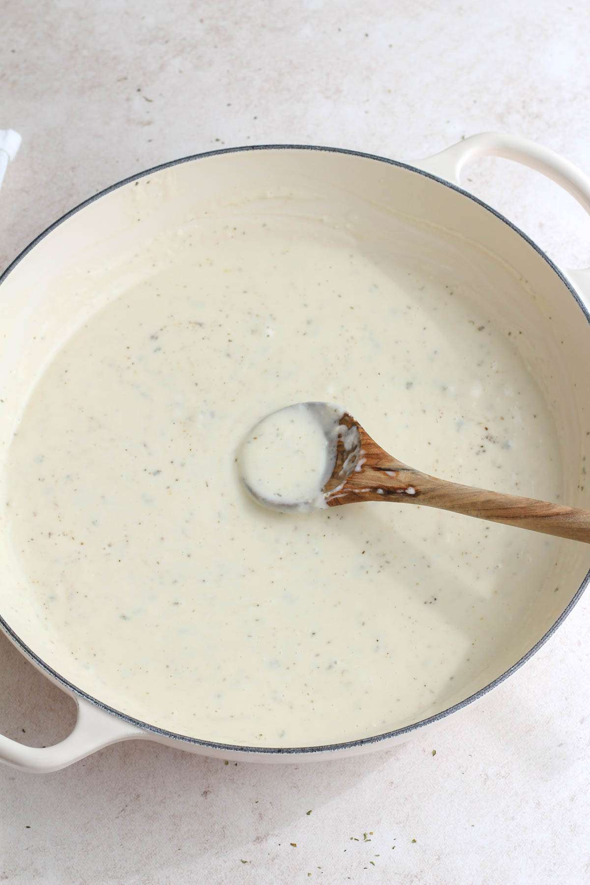 A white skillet with a wooden spoon in the vegan boursin sauce.