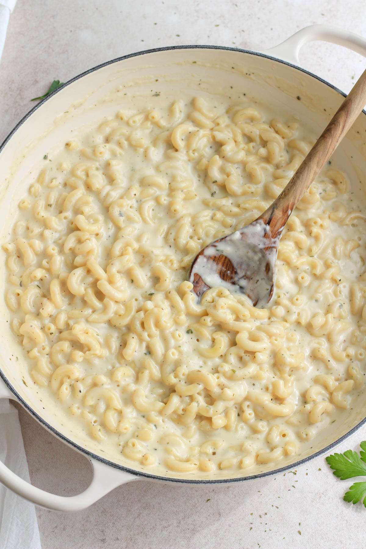 A top down image of a white skillet with a wooden spoon stirring the vegan boursin pasta.