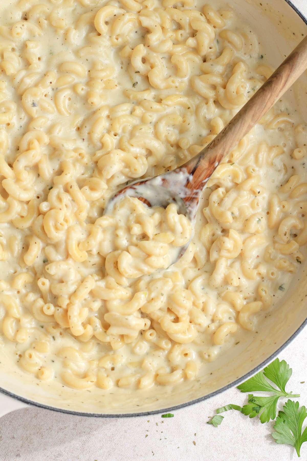 A white skillet with a wooden spoon scooping vegan boursin pasta from the pan.