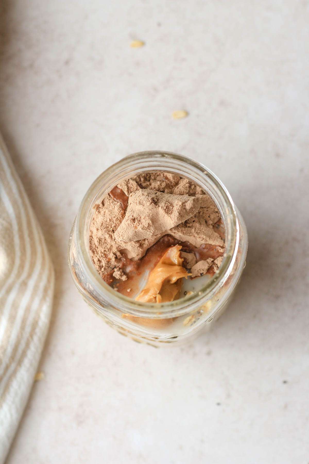 A top down image of a glass mason jar with the ingredients for chocolate peanut butter overnight oats before mixing.