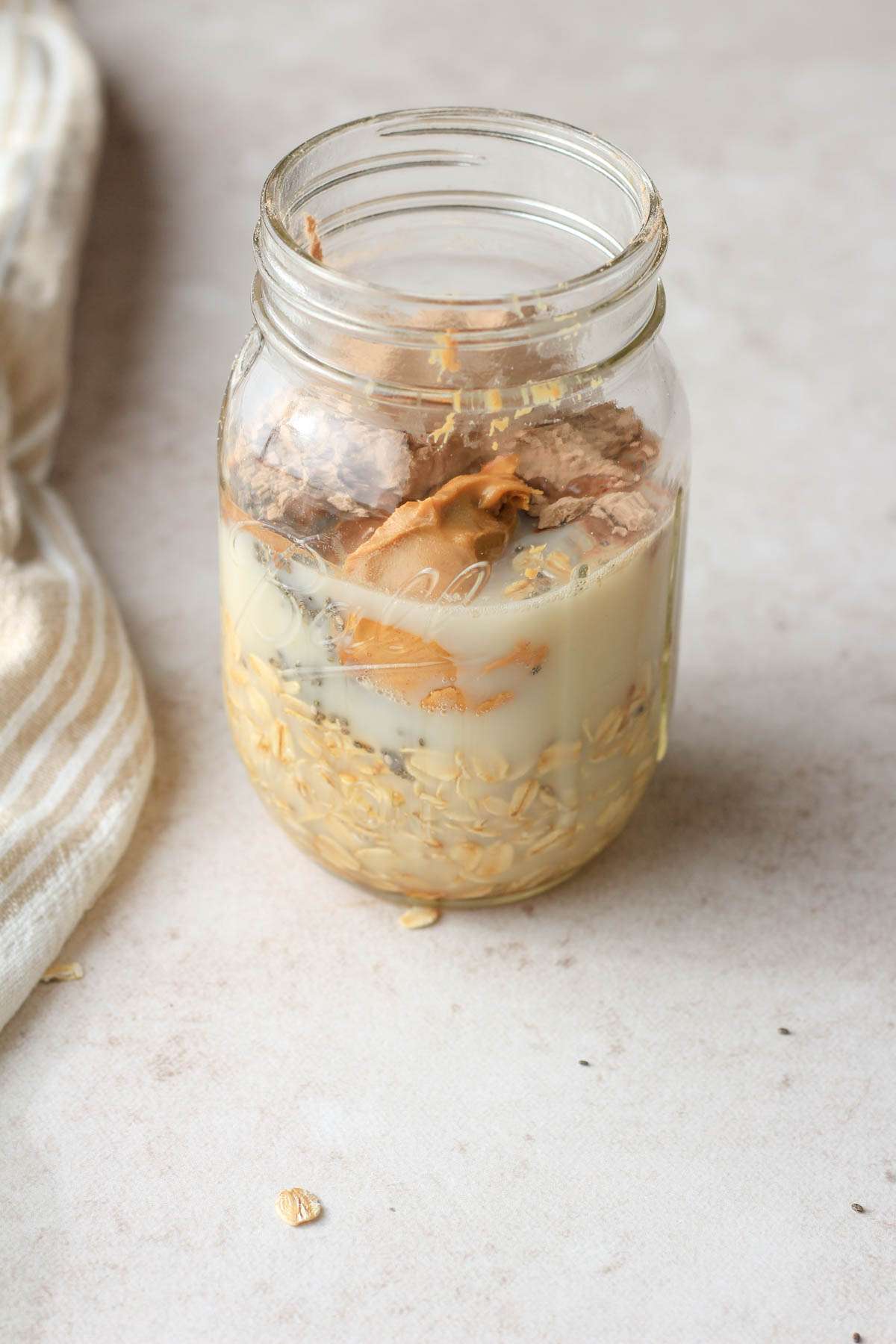 From the side, a glass mason jar with chocolate peanut butter overnight oats before mixing together.