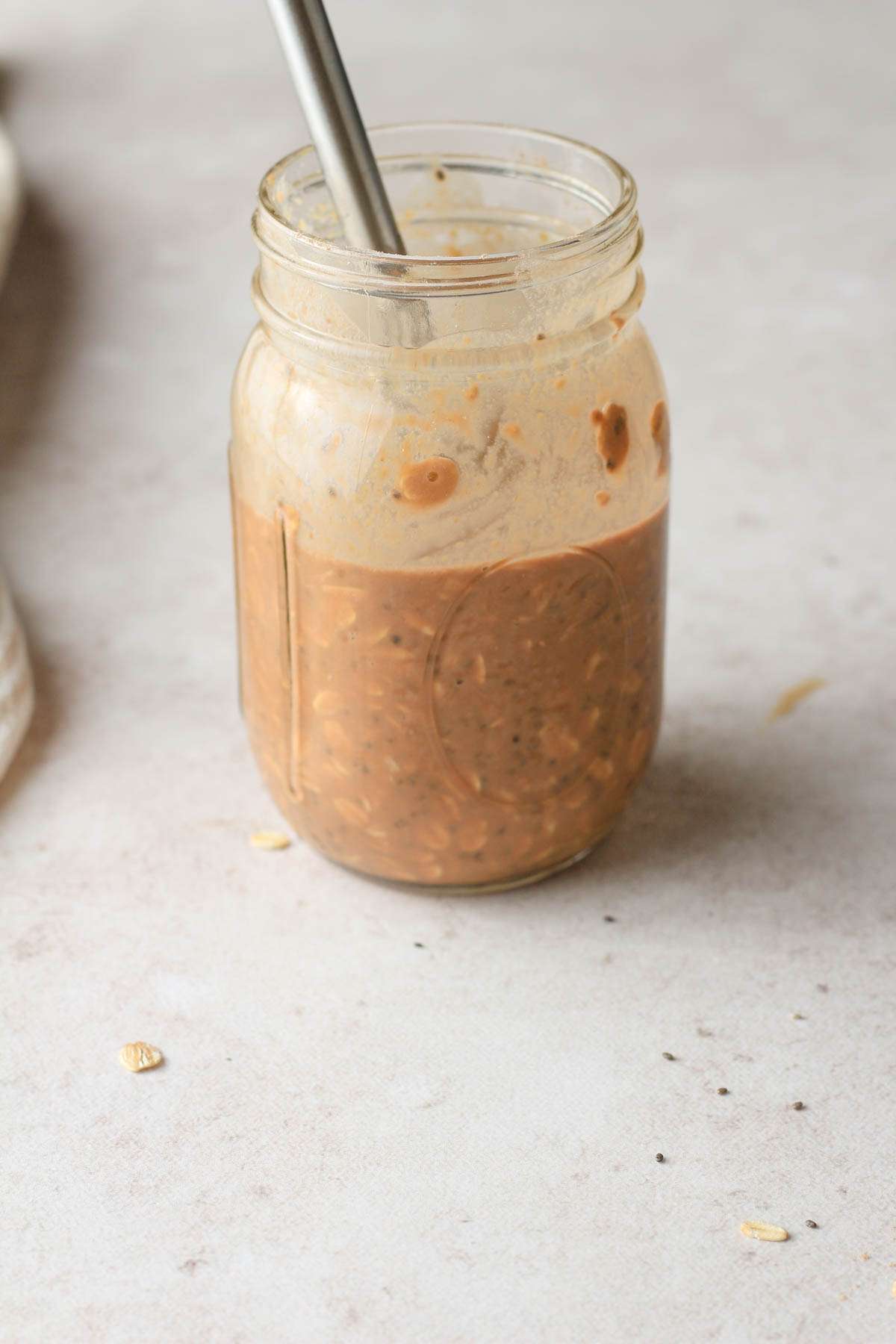 A glass mason jar with chocolate peanut butter overnight oats with a small whisk after mixing the oats together.