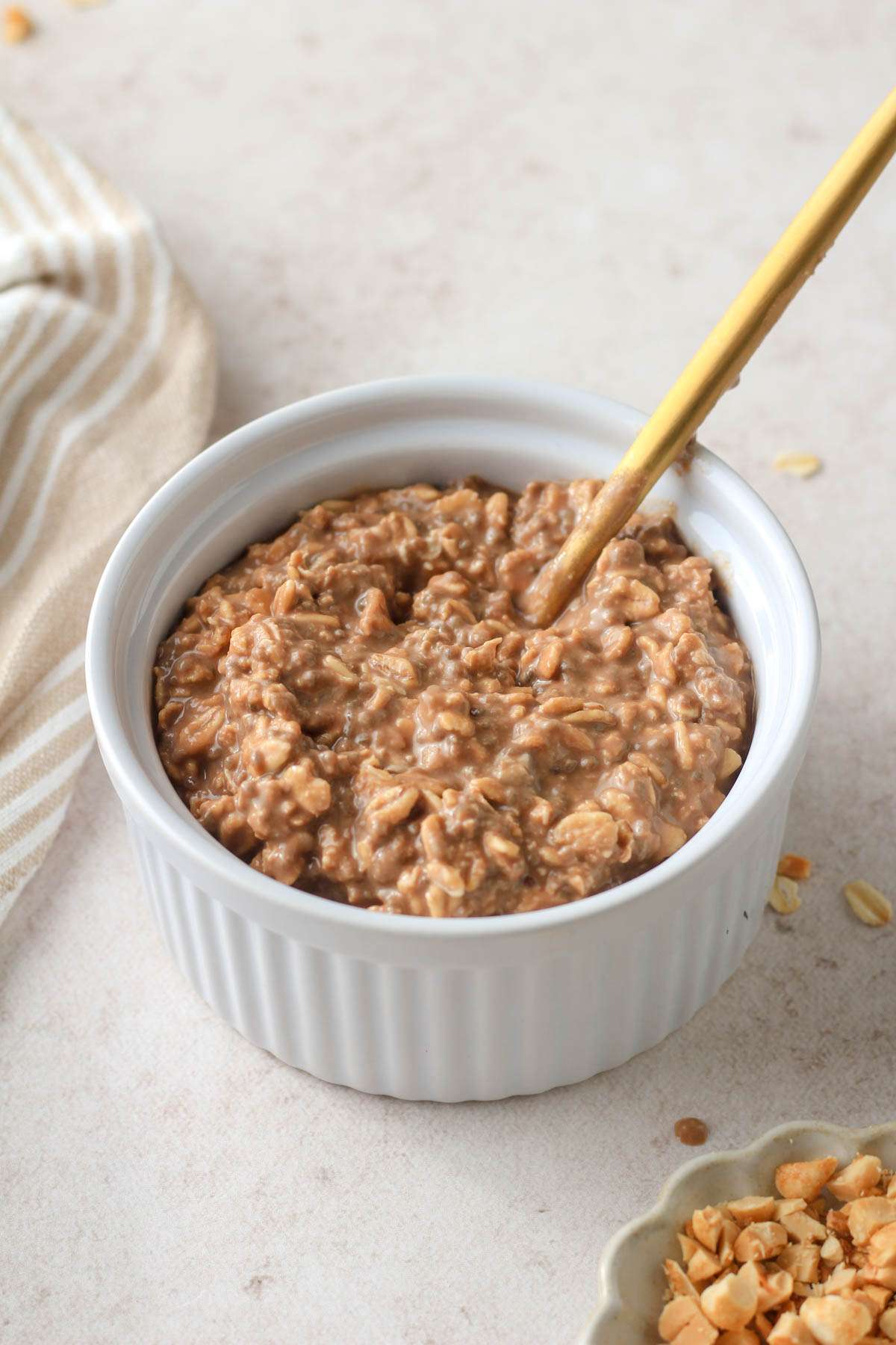 A white bowl with chocolate peanut butter overnight oats and a gold spoon in the back right of the bowl.