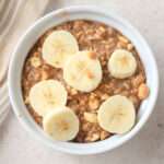 A top down image of chocolate peanut butter overnight oats in a white bowl topped with slices of banana.