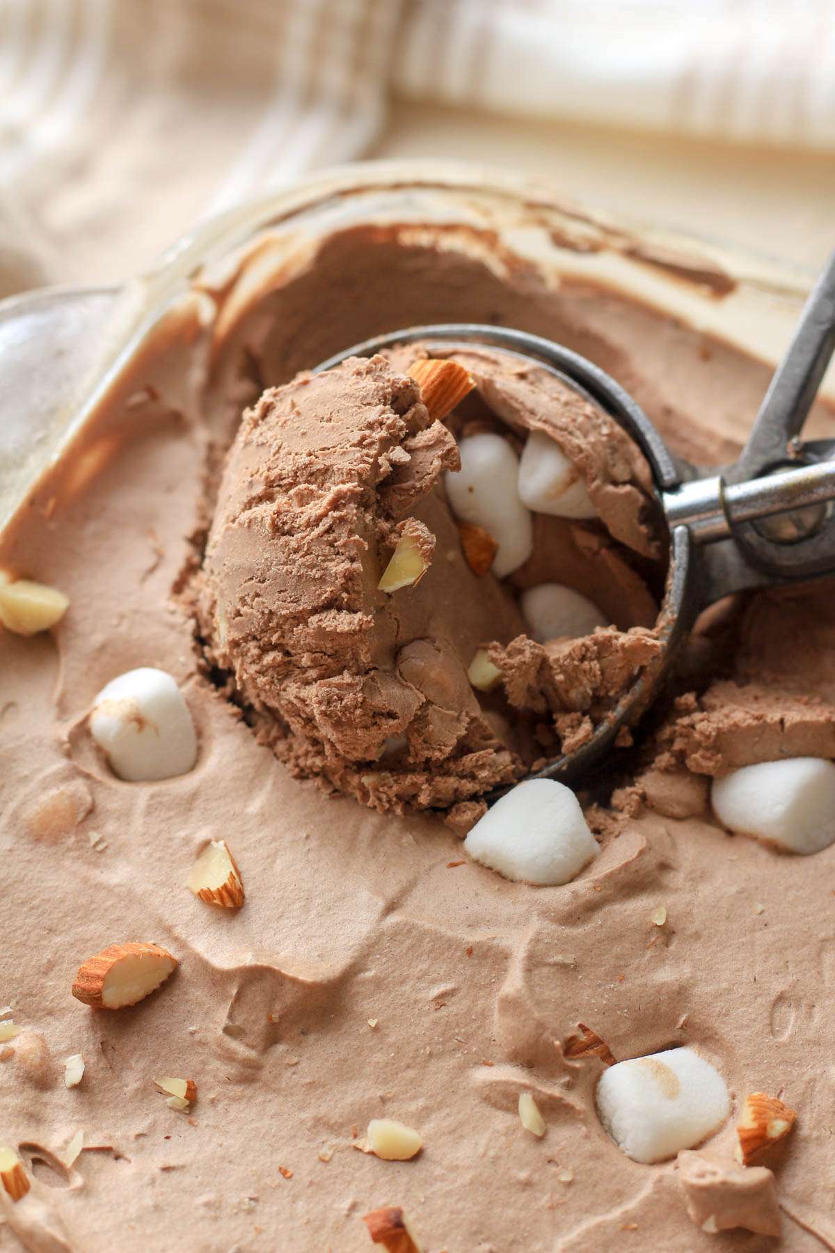 An ice cream scoop, scooping out a scoop of dairy free rocky road ice cream.