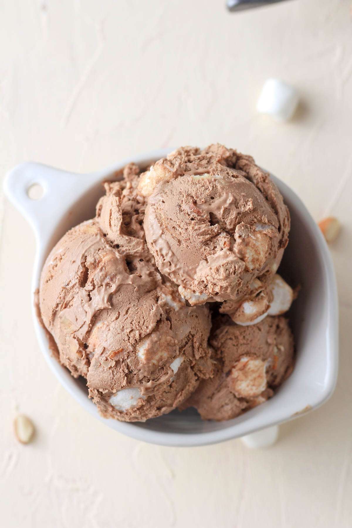 No churn rocky road ice cream in a white bowl on a cream counter with marshmallows and almonds.