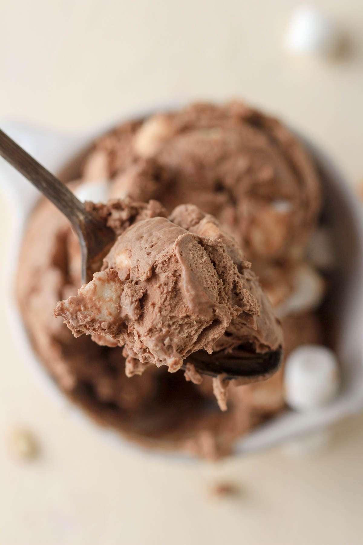 A silver spoon holding up a scoop of dairy free rocky road ice cream over a bowl of ice cream.